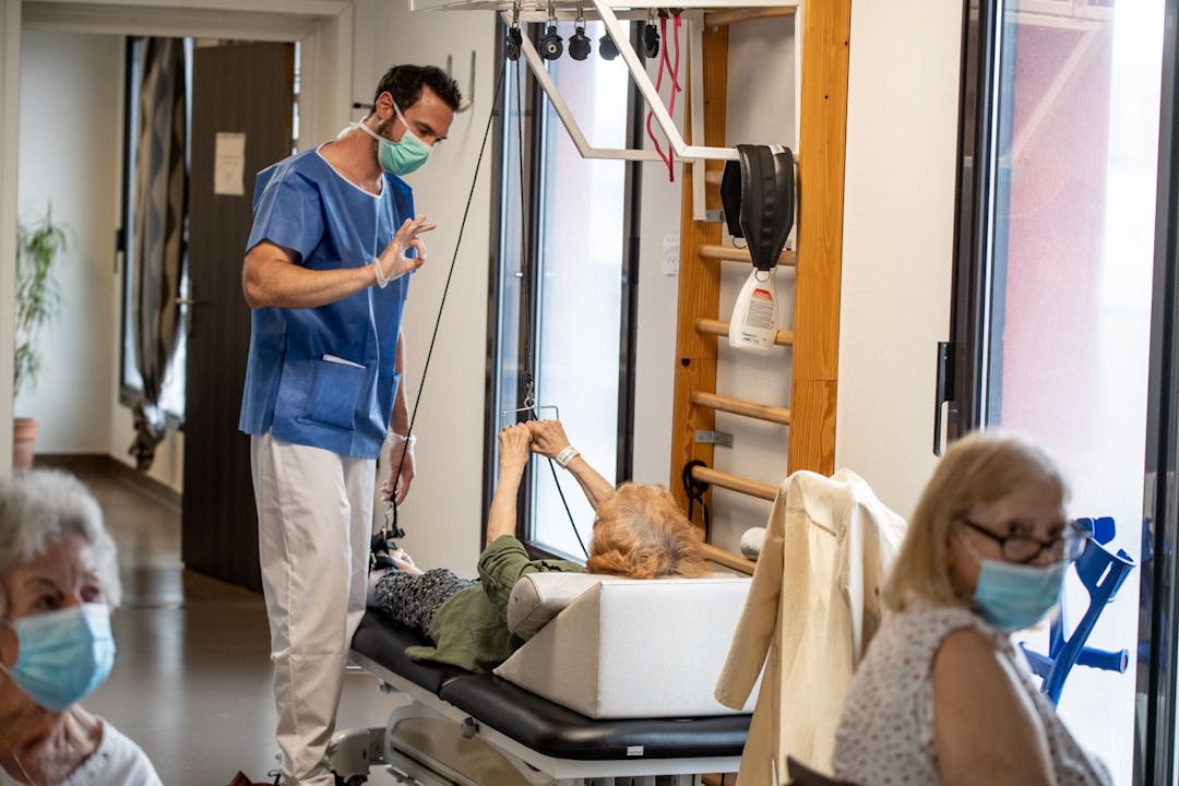 Photo illustrant une patiente réalisant un exercice de réeducation, accompagnée de son réeducateur au sein de la clinique des minimes